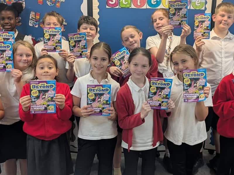 A group of school children in class holding copies of The Beyond Comic